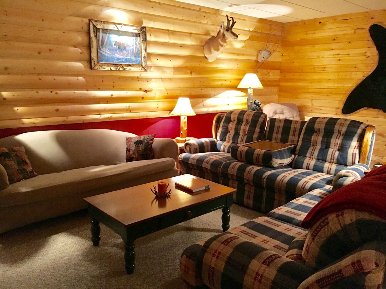 Cozy up in this rustic living room with plaid furniture, warm wood walls, and gentle lamplight for relaxing evenings.