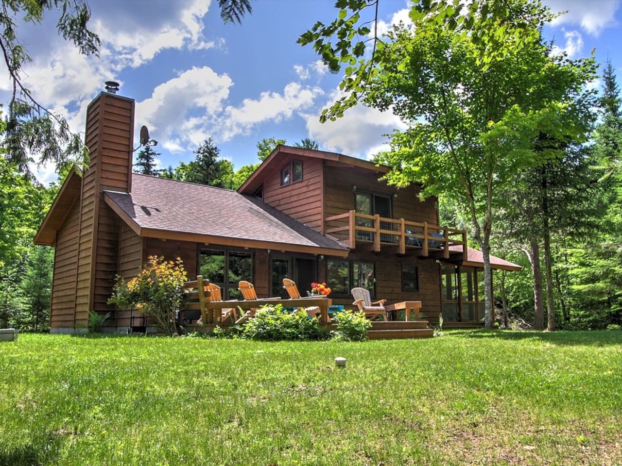 A beautiful cedar cabin nestled among mature trees with spacious decks and manicured lawn in a peaceful woodland setting.