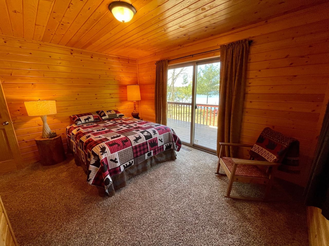 Cozy cabin bedroom with warm wood walls where you'll drift off under soft quilts, then wake to natural light streaming through your private balcony doors.