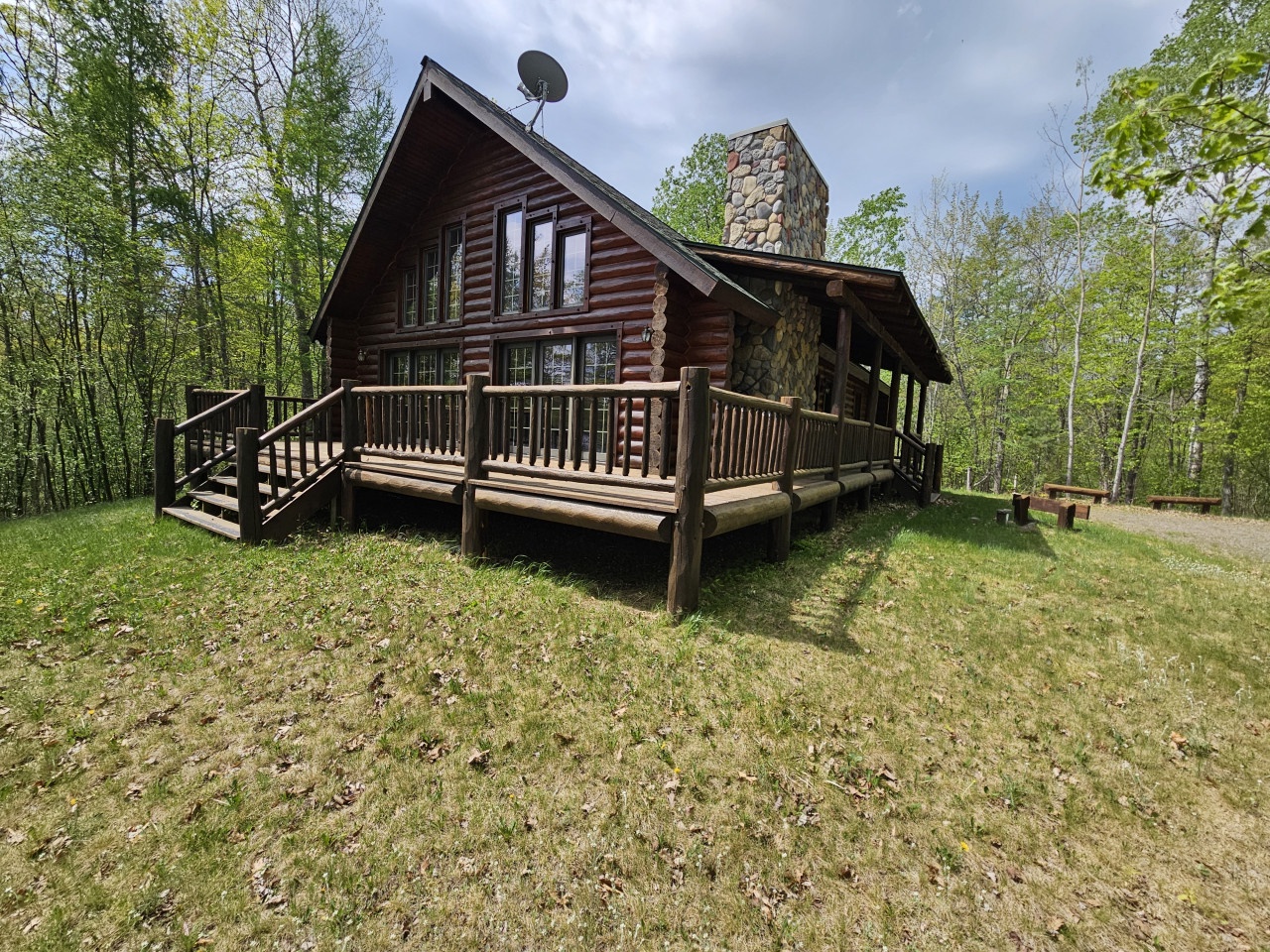 A rustic log cabin nestled among towering trees features a wraparound deck and stone chimney for your perfect woodland retreat.