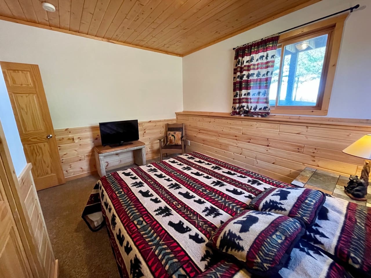 Cozy rustic bedroom with warm wood paneling and charming bear-themed bedding creates your perfect mountain retreat sanctuary.