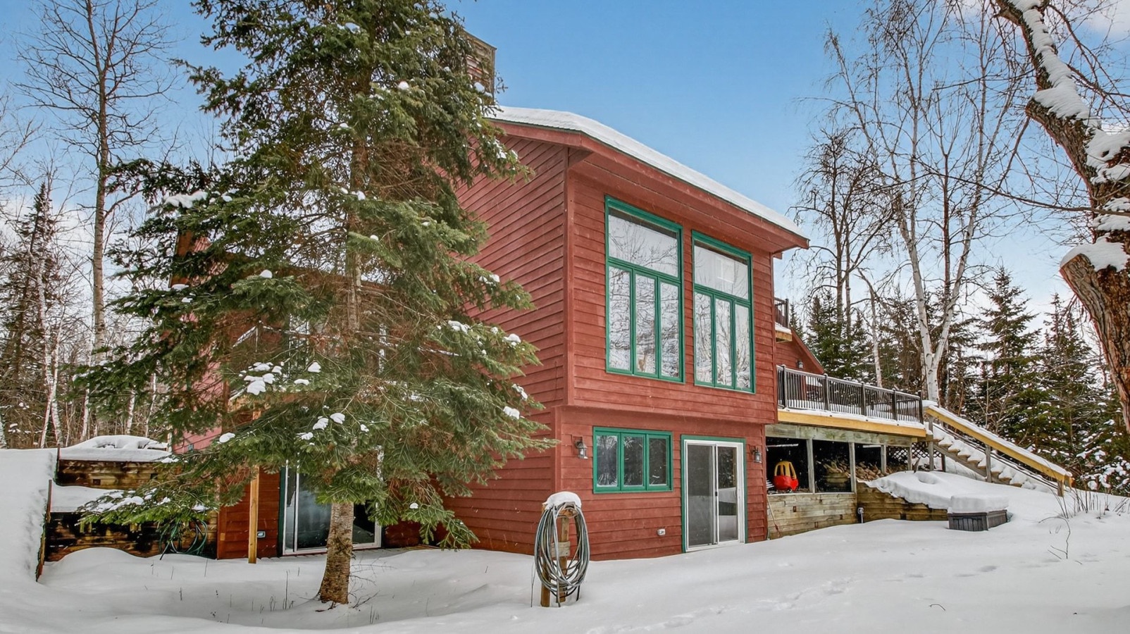 Modern cabin nestled among snow-covered evergreens, featuring warm wood siding and expansive windows with elevated deck access.