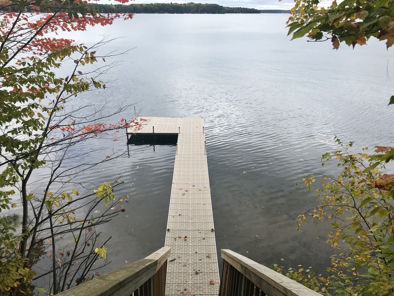 Private dock stretches into pristine lake waters, surrounded by vibrant autumn foliage and peaceful shoreline views.