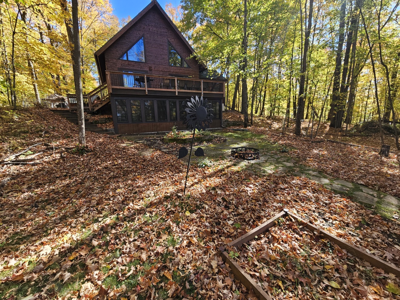 Charming A-frame cabin nestled among vibrant autumn trees with outdoor fire pit perfect for cozy fall evenings.