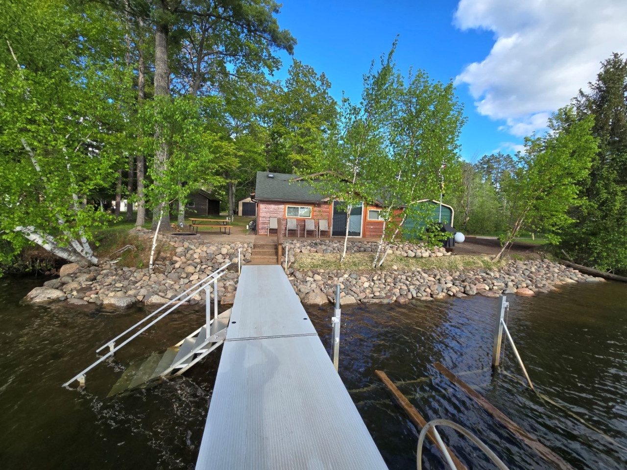 Waterfront cabin with private dock nestled among towering trees on pristine lake waters.