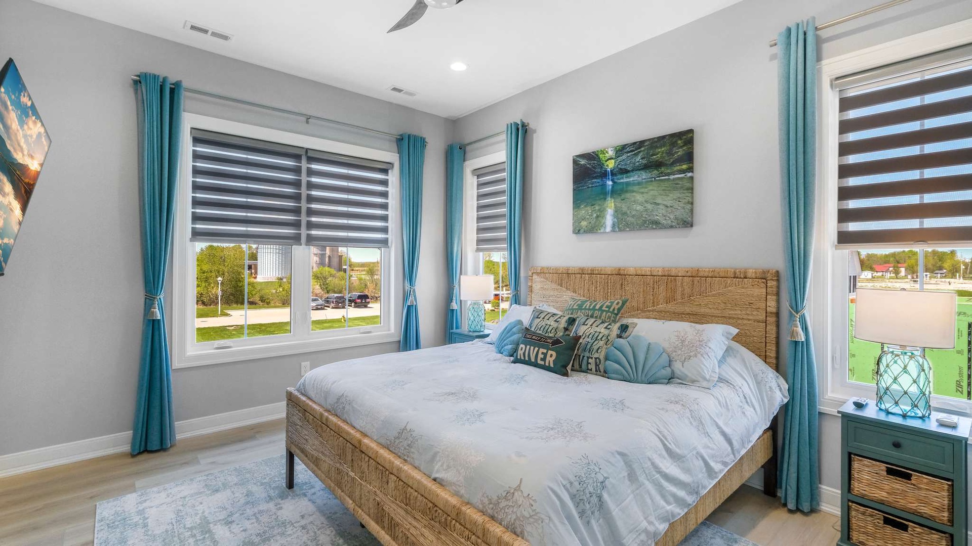 Drift off in this serene bedroom with woven headboard, nature art, and calming turquoise accents framing peaceful neighborhood views.