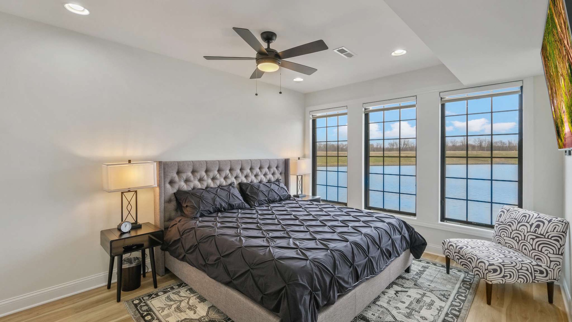 Drift off in this elegant bedroom where natural light flows through expansive windows and a gentle ceiling fan creates the perfect sleeping environment.