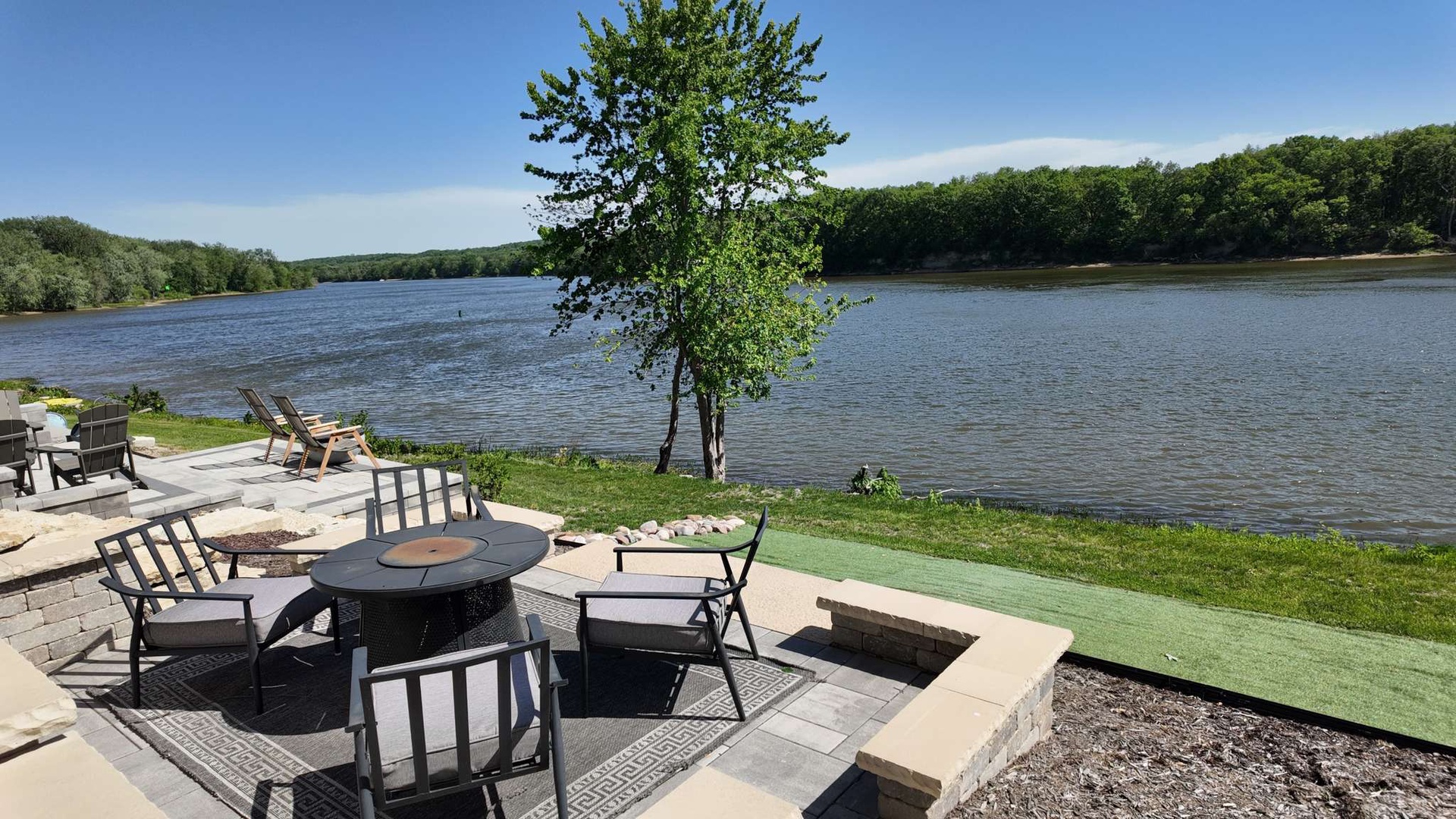 Relax by your private lakefront with cozy seating around the fire pit, where peaceful waters and lush greenery create the perfect escape.