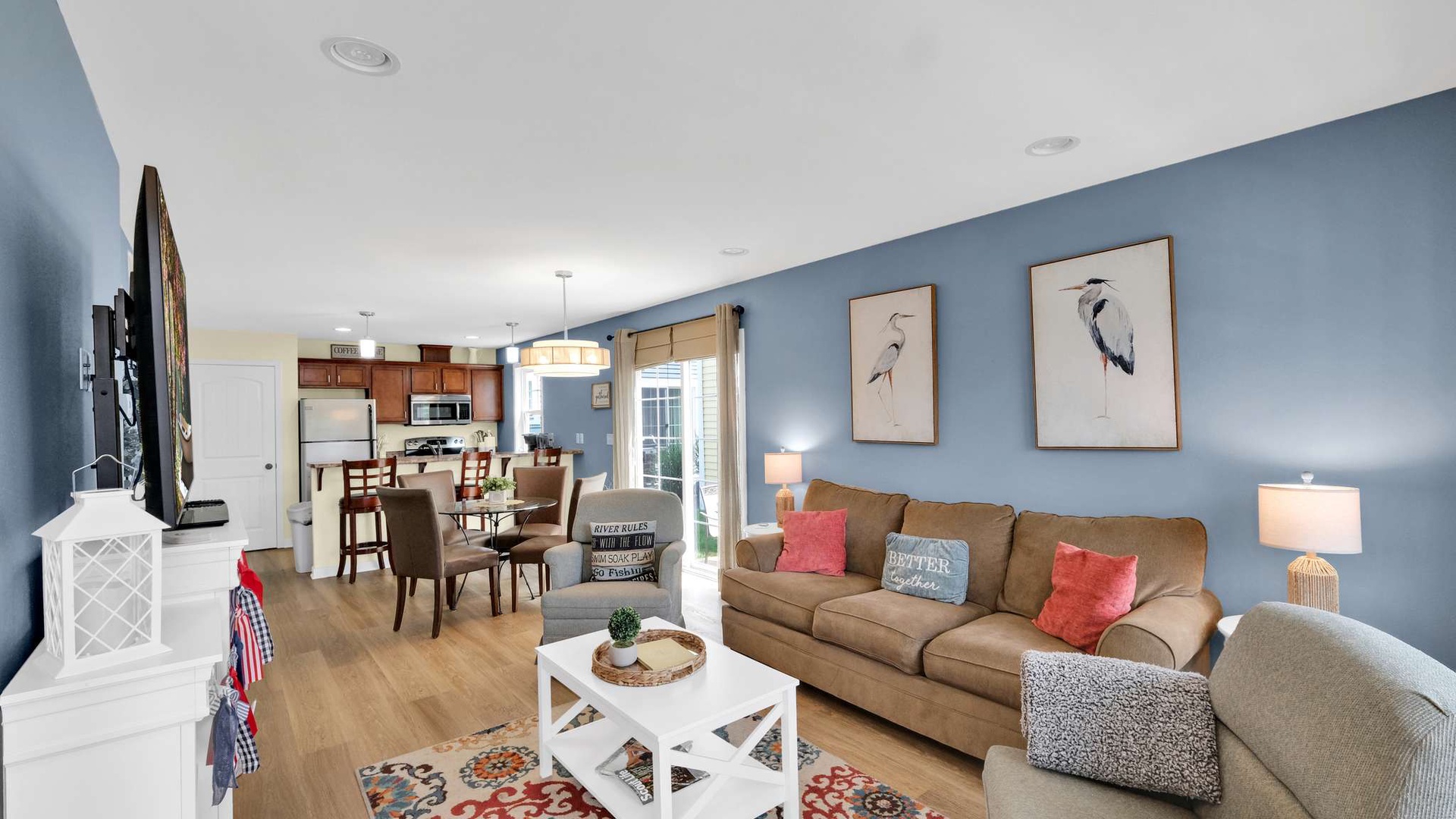 Relax in your spacious open-concept living space with plush seating, coastal artwork, and a fully equipped kitchen perfect for memorable meals.