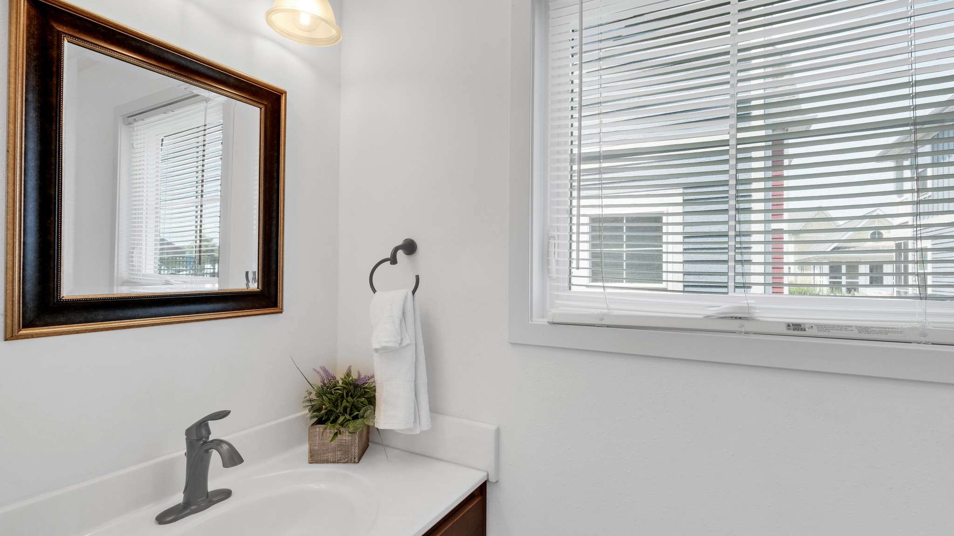 Fresh white bathroom with natural light streaming through blinds, elegant mirror, and soft towels ready for your arrival.