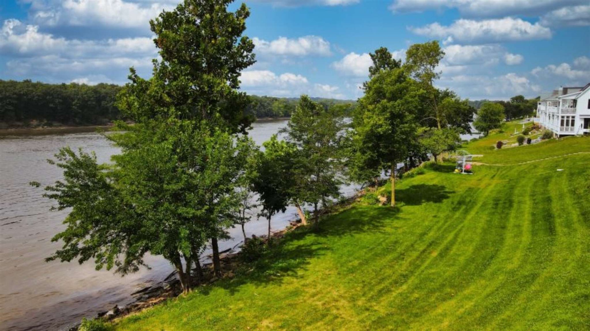Waterfront property featuring expansive lawns leading to the river, mature trees, and scenic surroundings perfect for a peaceful getaway.