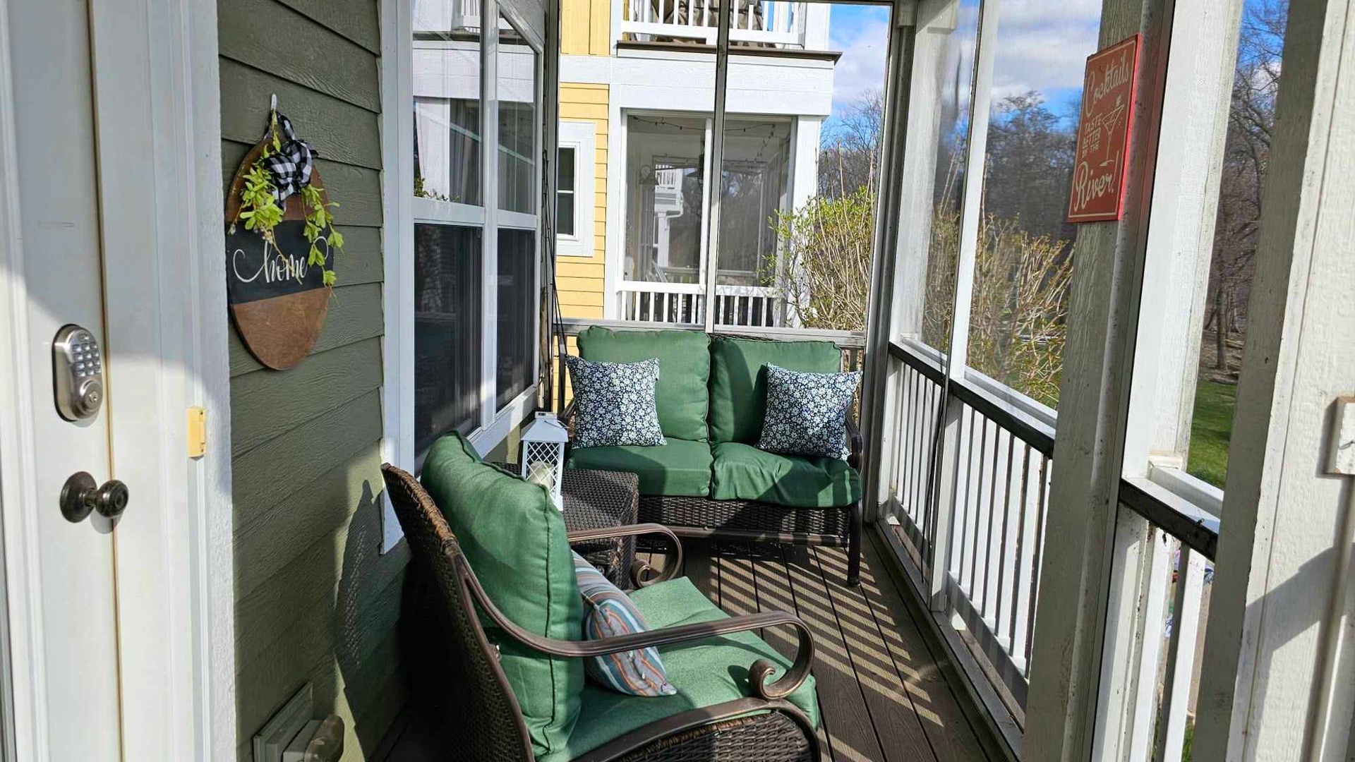 Relax on your screened porch with comfortable green seating, perfect for morning coffee or evening conversations in this peaceful neighborhood setting.