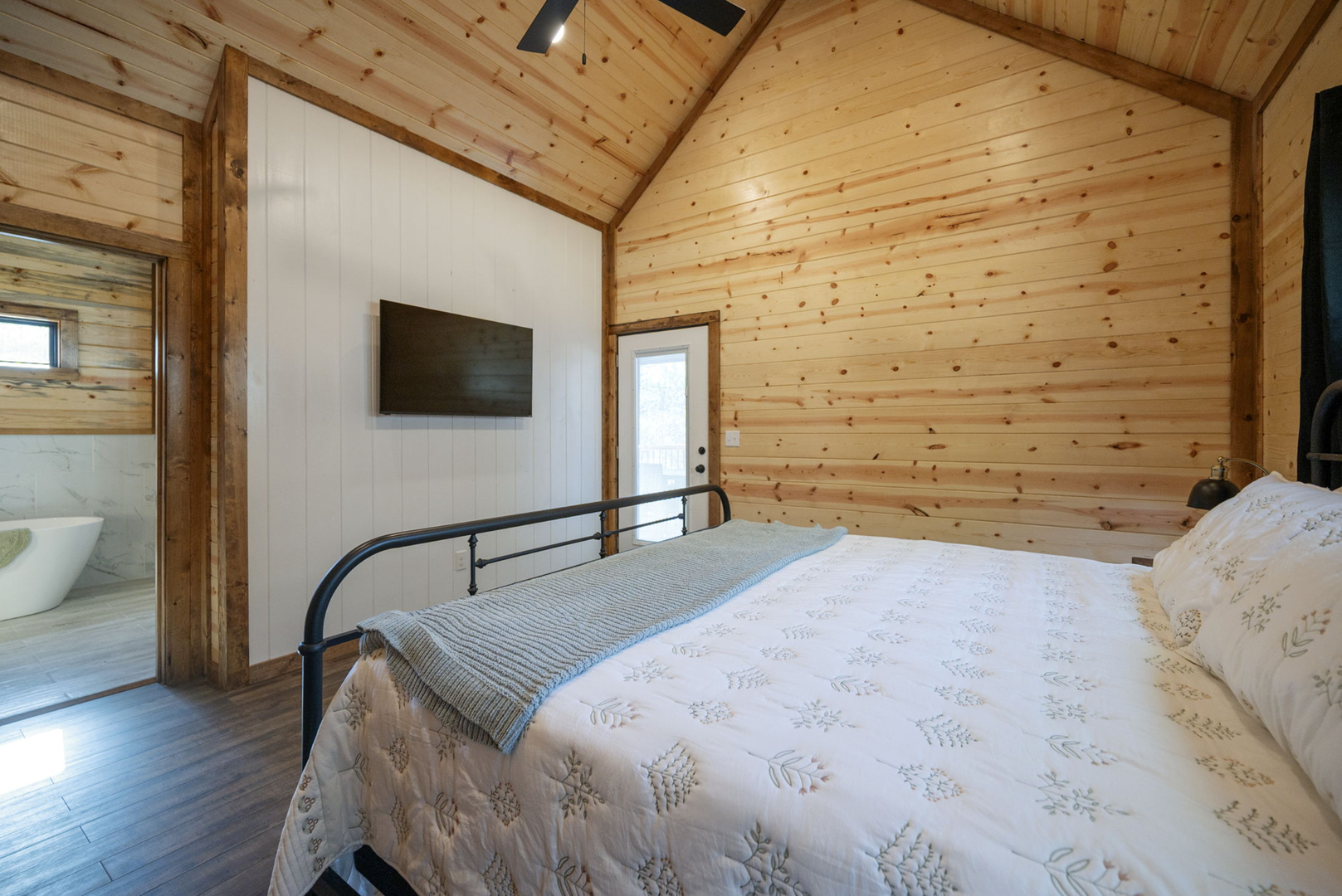 Your cozy bedroom features warm wood-paneled walls, crisp linens, and modern amenities for a peaceful mountain retreat.