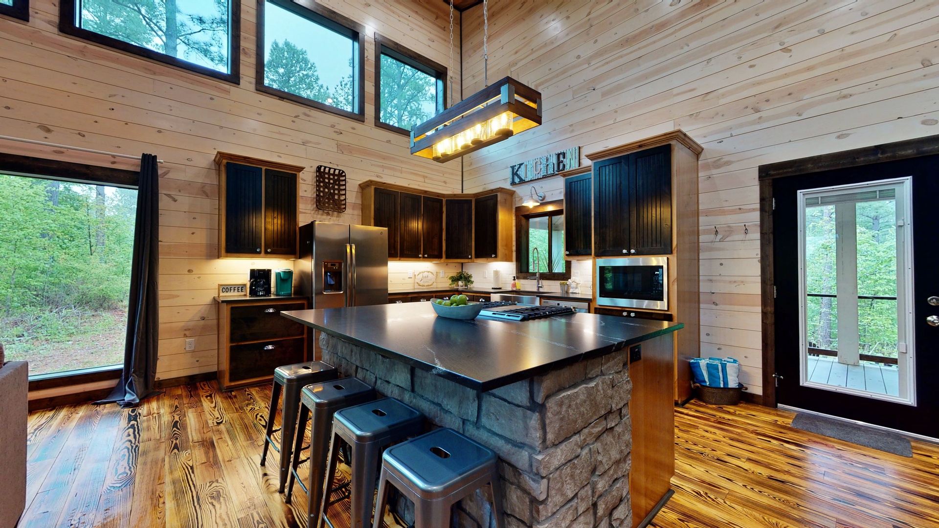 Step into your rustic-modern retreat, where natural light streams through soaring windows and warm wood surrounds you. The gourmet kitchen features a striking stone island, perfect for preparing meals and gathering over morning coffee.