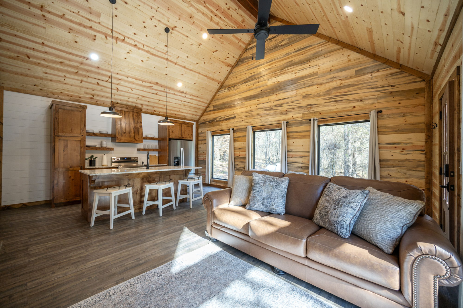 Unwind in this cozy log cabin retreat with vaulted ceilings and rustic charm flowing from kitchen to living space.