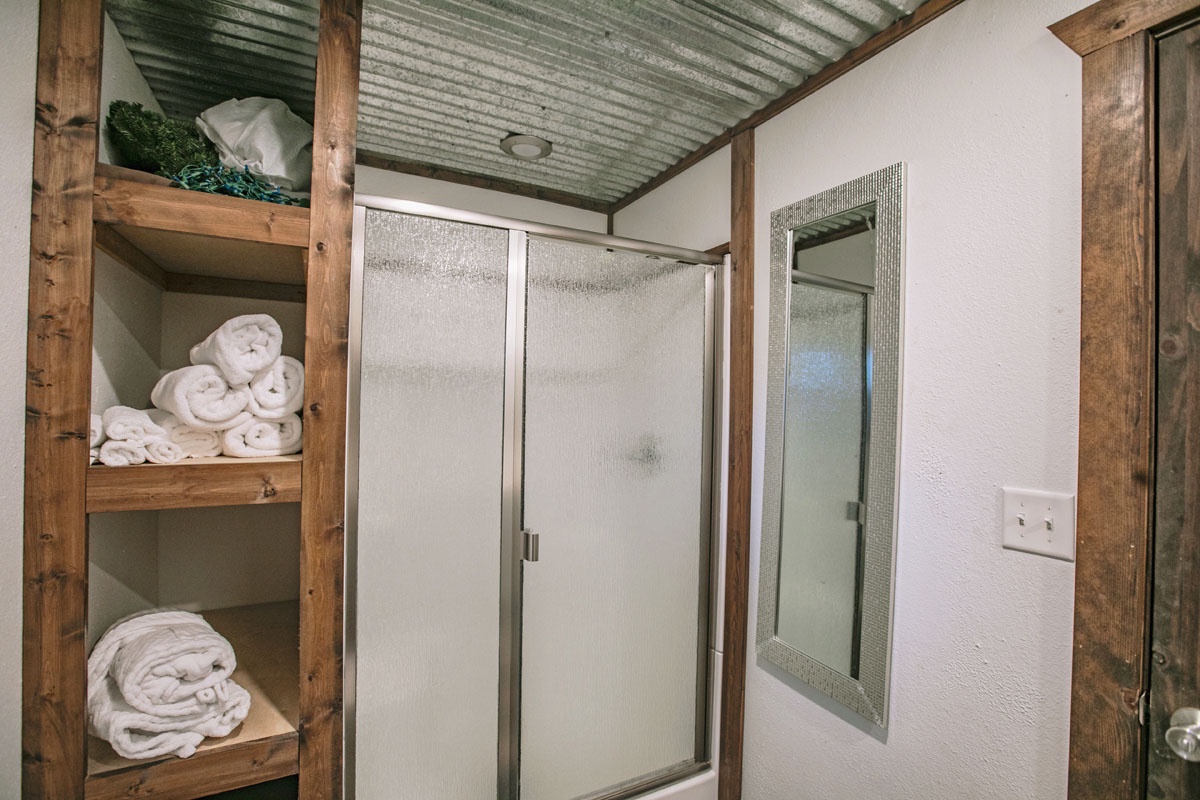 Fresh towels await you in this rustic bathroom with warm wood accents and a spacious glass-enclosed shower.