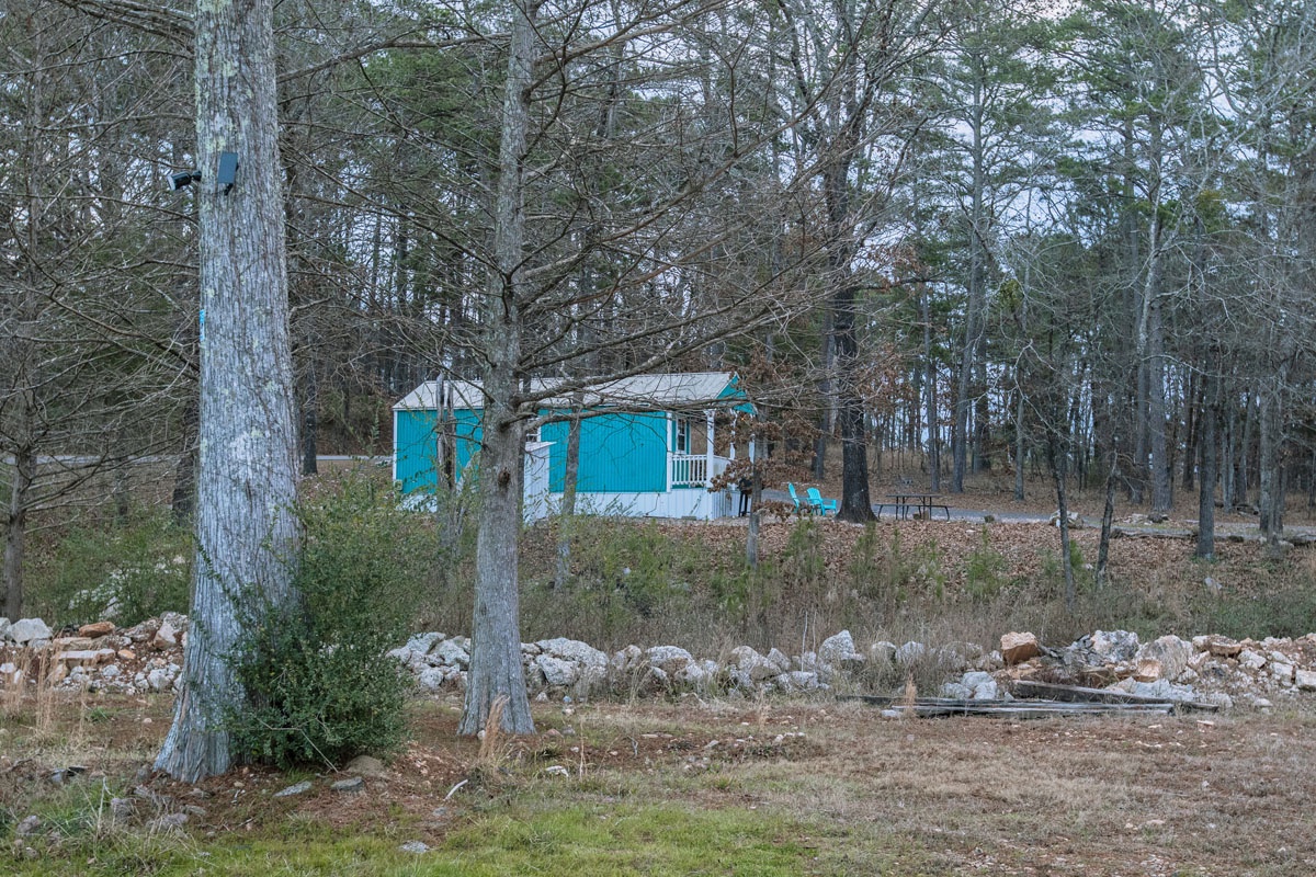 Charming blue cottage nestled among mature trees in a peaceful wooded setting with natural stone features.