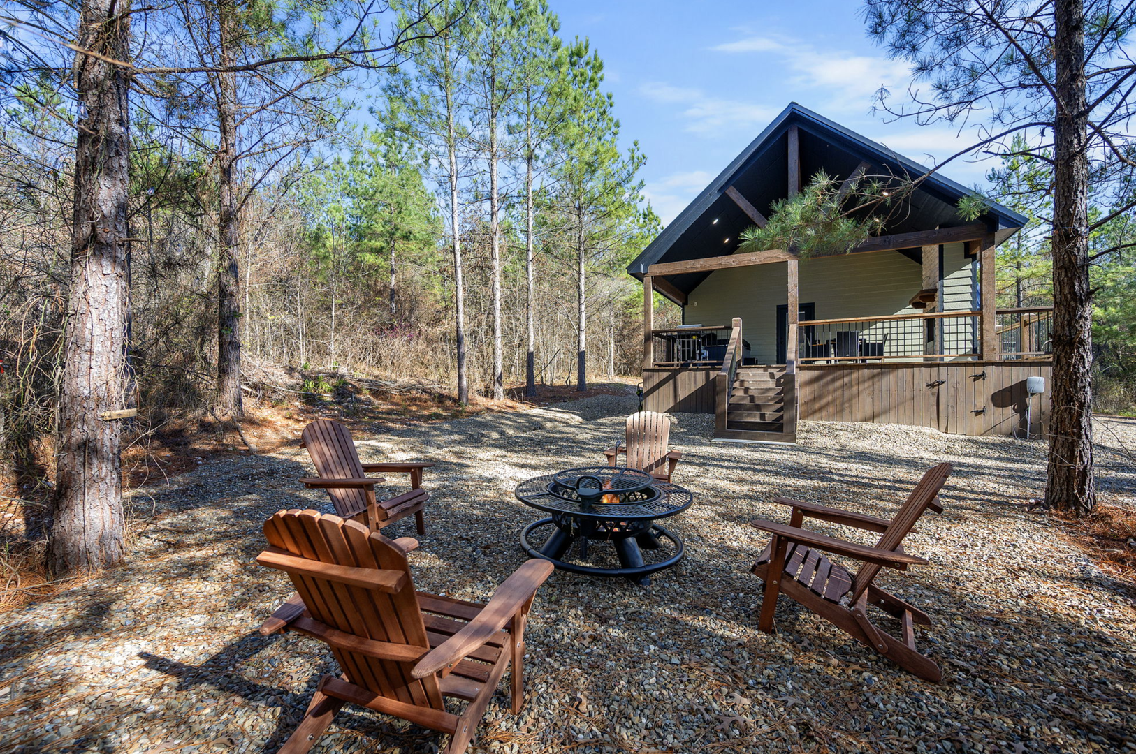 Modern cabin retreat nestled among towering trees with covered deck and fire pit seating area surrounded by peaceful forest.