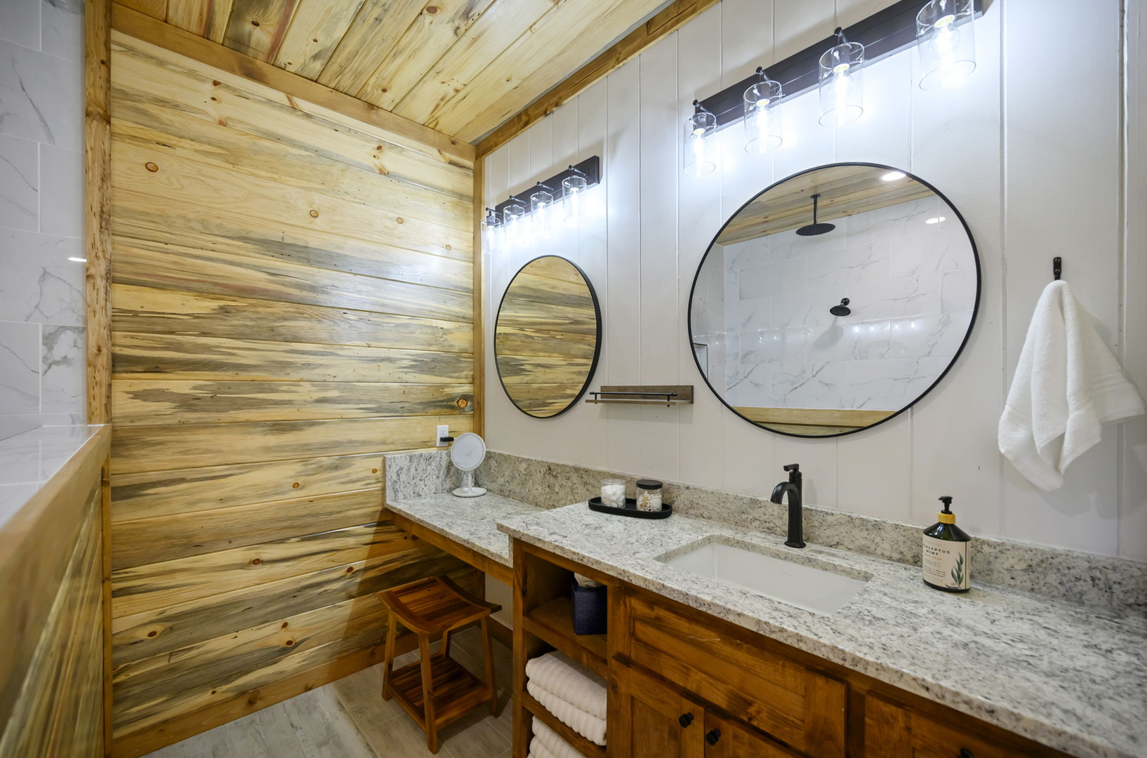 Refresh in your beautifully appointed bathroom featuring warm wood accents, marble countertops, and stylish round mirrors.