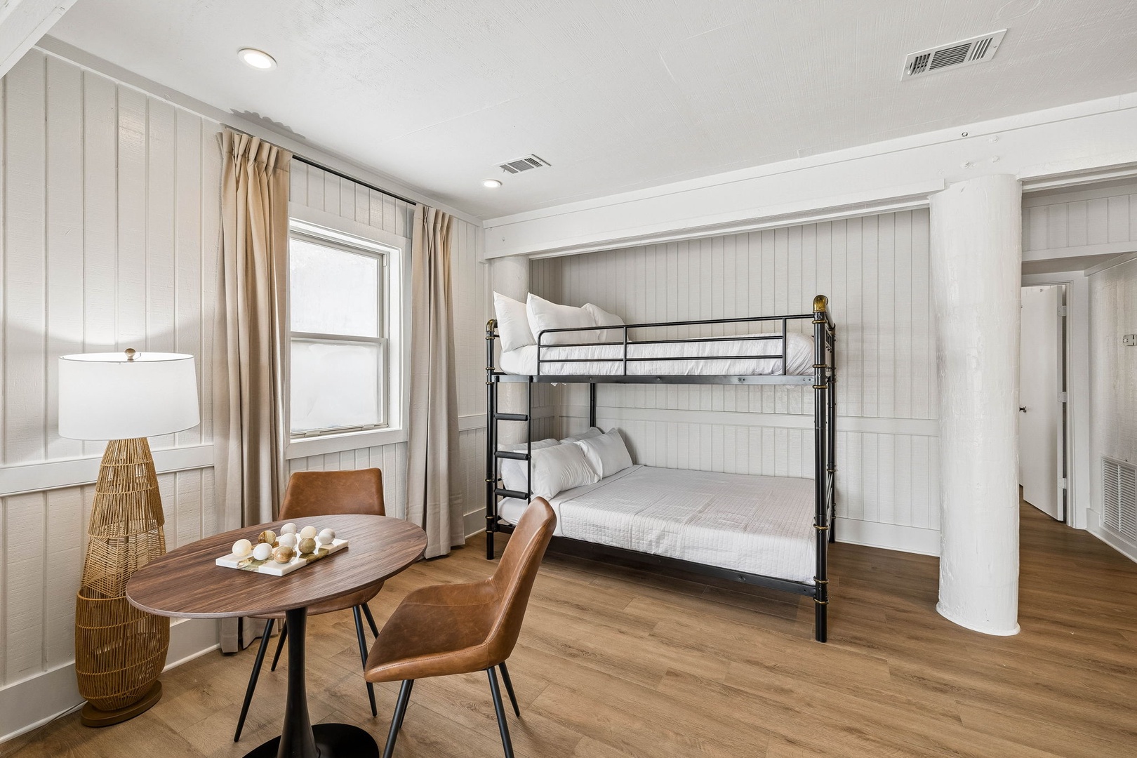 Your bright, inviting room features cozy bunk beds with crisp linens, warm wood floors, and a charming table for two—perfect for morning coffee or quiet moments.