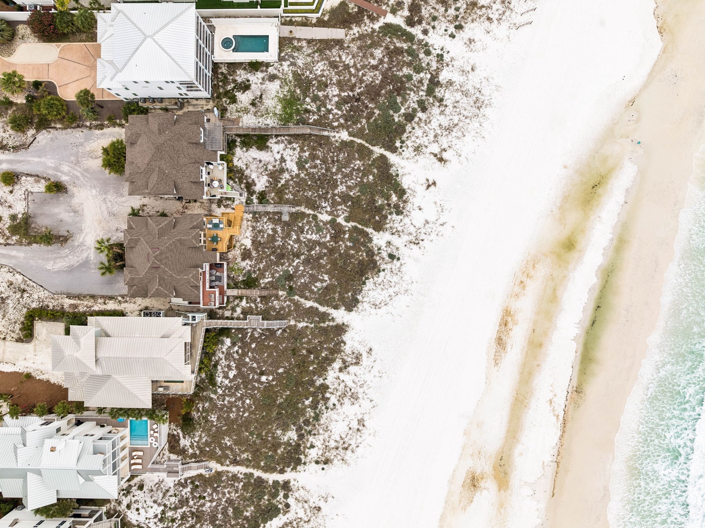 Aerial view of beachfront vacation homes nestled between coastal vegetation and pristine white sand beaches, with turquoise waters nearby.