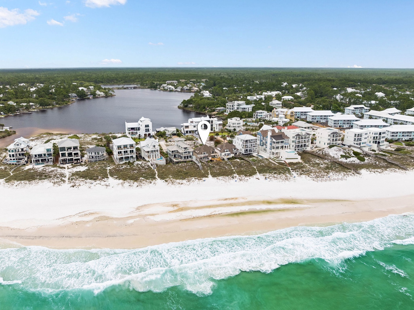 Aerial view showcasing pristine white-sand beaches meeting emerald Gulf waters, with coastal vacation homes nestled between the shoreline and a tranquil inland waterway surrounded by lush greenery.