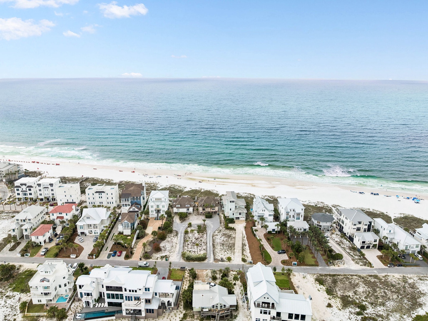 An aerial view captures the pristine coastal community featuring white-sand beaches and turquoise waters of the Gulf. A collection of modern beach homes nestles among native dunes and vegetation.