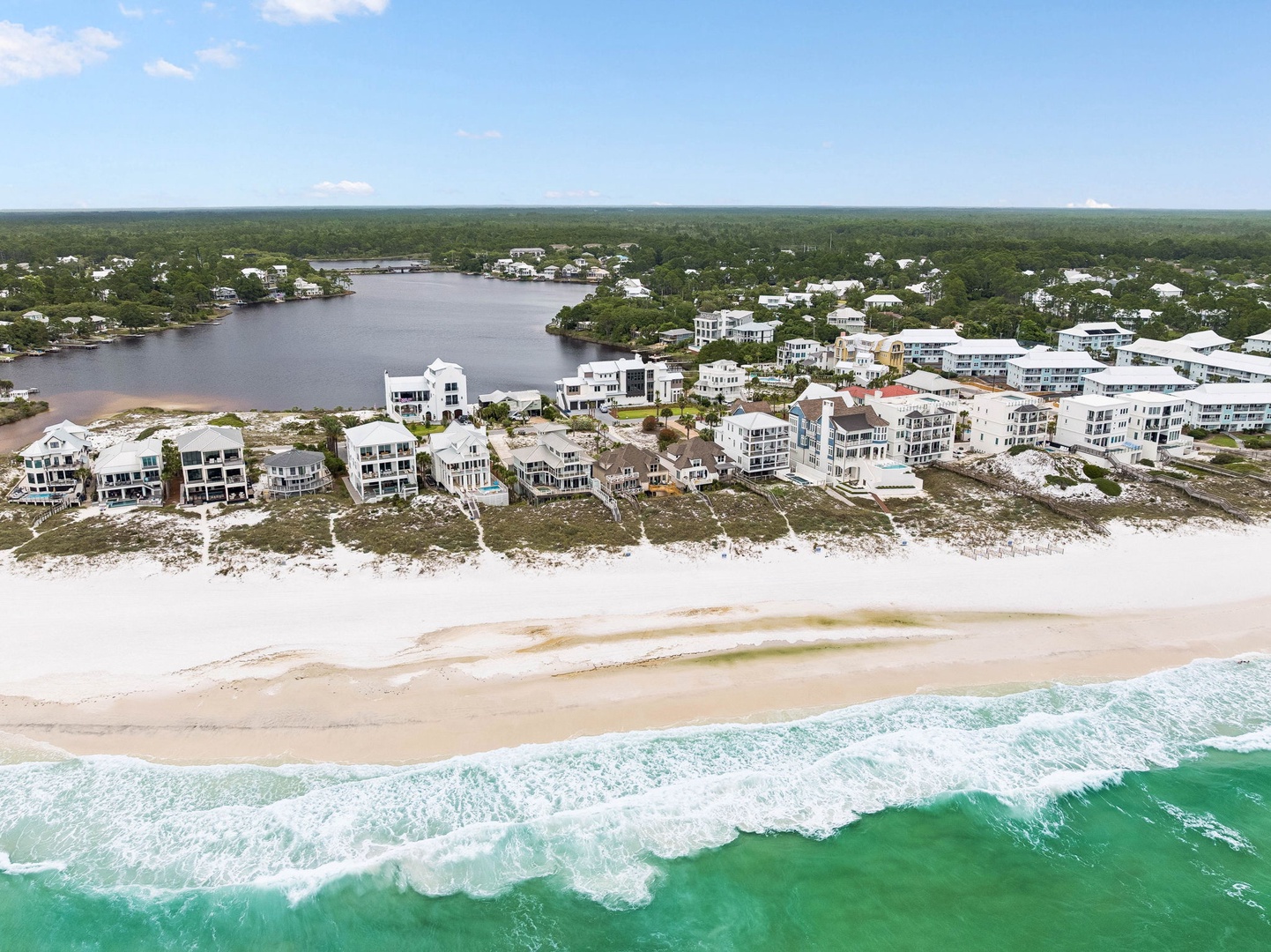 Aerial view showcasing beachfront vacation properties nestled between pristine emerald Gulf waters and a serene inland lagoon, surrounded by natural coastal landscape.