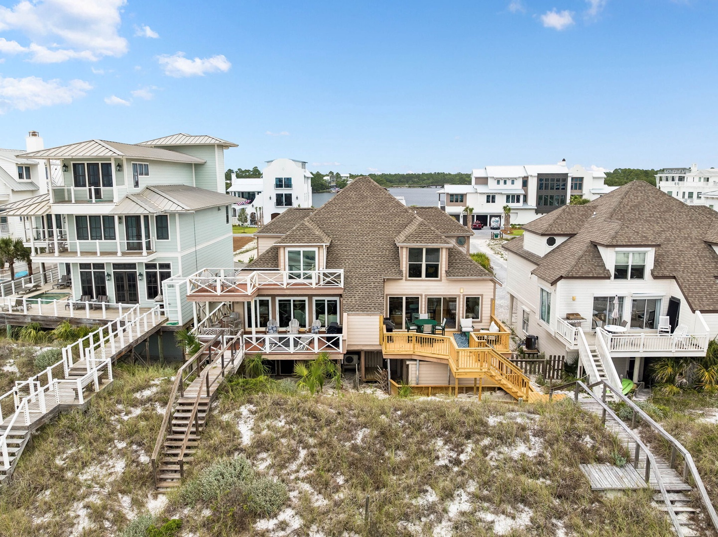 Aerial view showcasing beachfront vacation homes with private boardwalks leading through natural dunes to the shore, situated in a coastal community with nearby amenities.