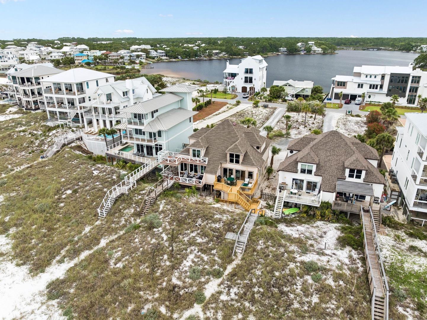 Aerial view of the waterfront property nestled in a coastal neighborhood with expansive lake views and sandy terrain leading to private boardwalk access.
