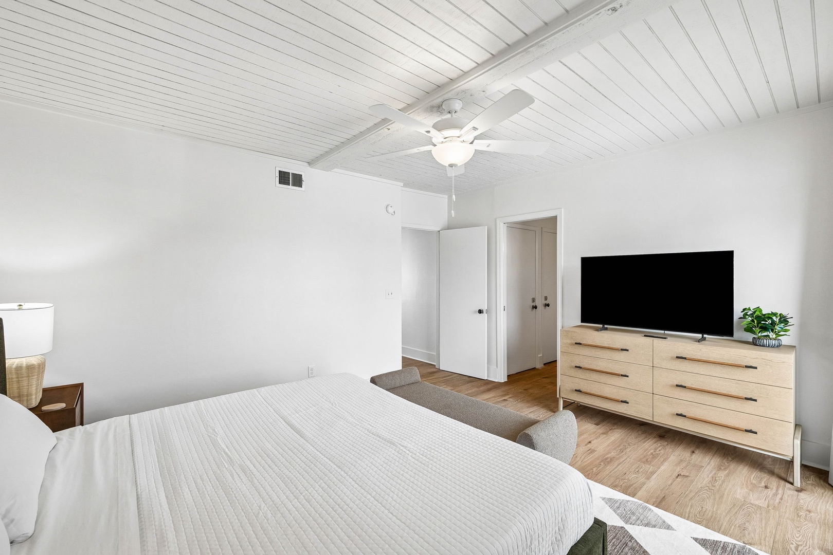 Unwind in your bright, airy bedroom featuring elegant wood ceiling, stylish furnishings, and modern TV for your evening relaxation.