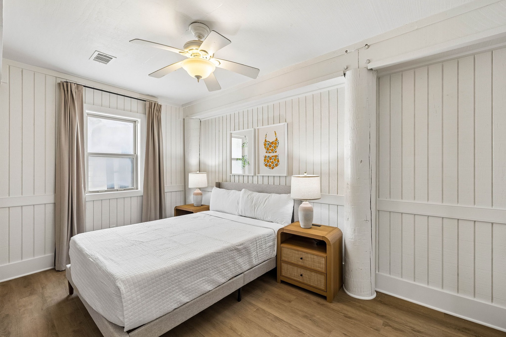 Sink into crisp white linens in this serene coastal-inspired bedroom, where natural light and the gentle whir of the ceiling fan promise peaceful nights.
