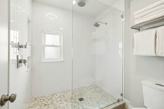 Step into your private spa-like retreat with a sleek walk-in shower featuring pebble flooring and rainfall showerhead, designed for your ultimate relaxation.