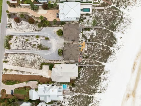 Aerial view of the property and its coastal surroundings, showcasing the vacation rental's proximity to natural sandy terrain and neighboring residences.