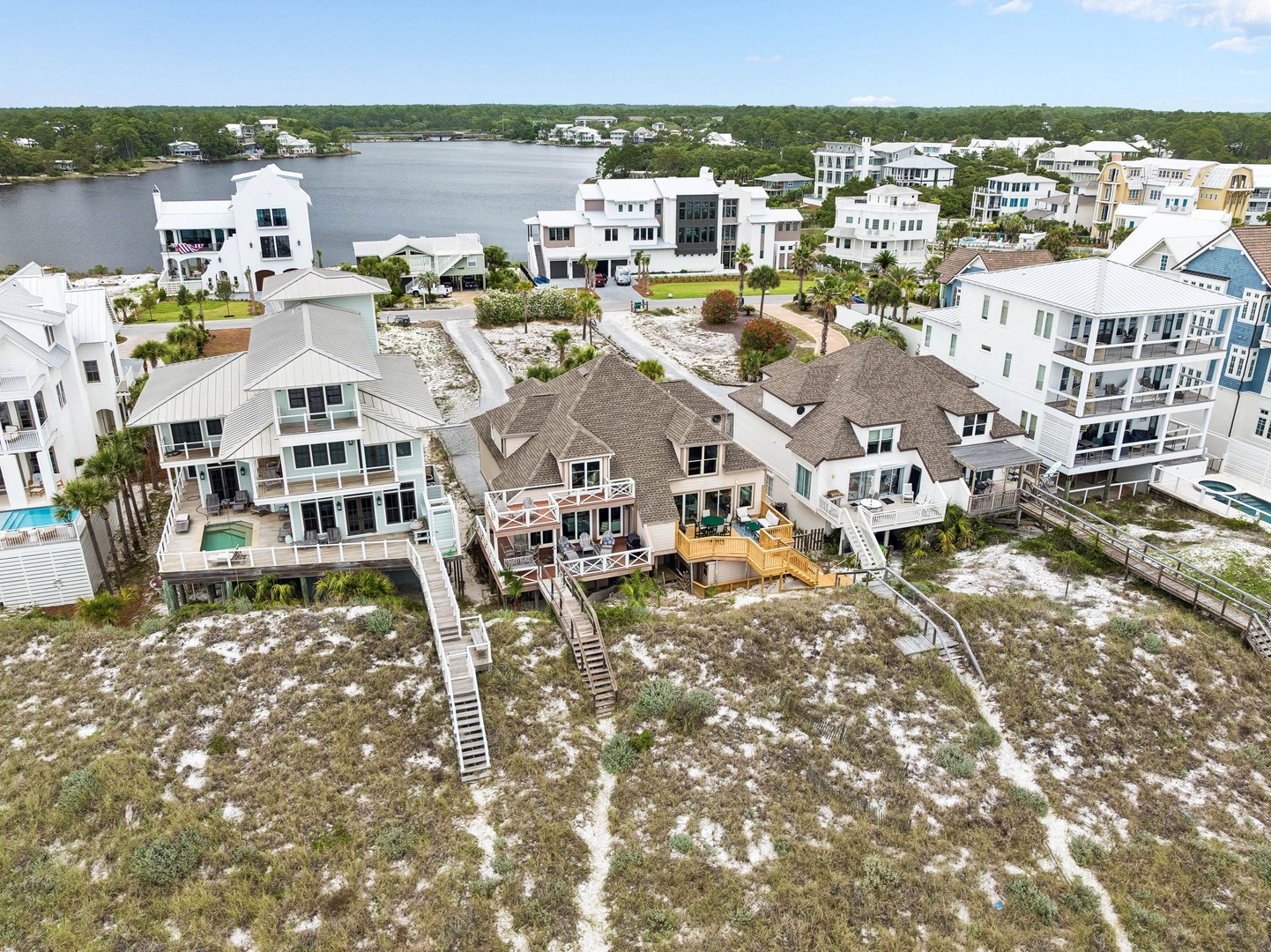 Aerial view of a coastal vacation community featuring lakefront homes with beach access, surrounded by natural dunes and lush greenery.