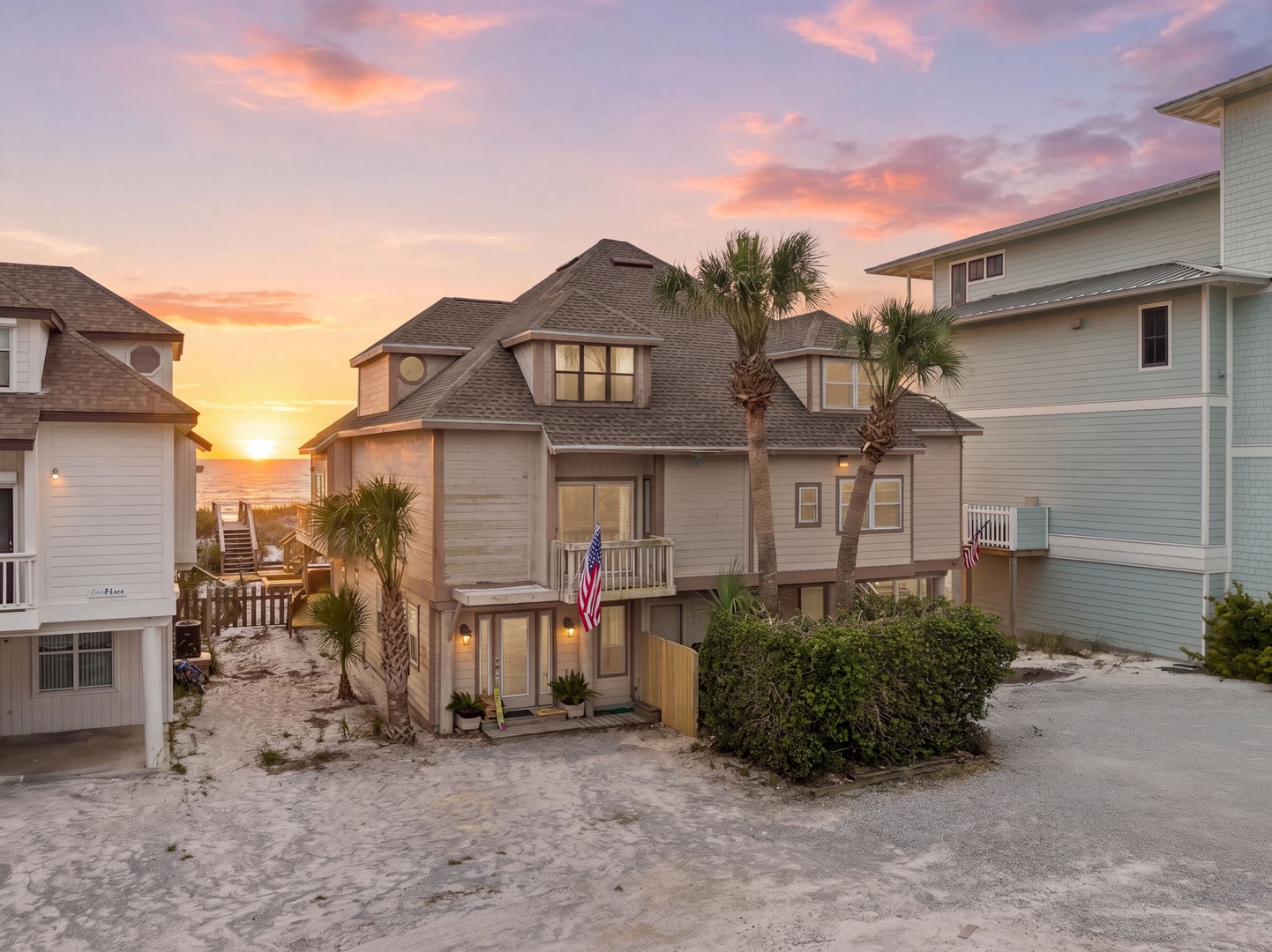 A beachfront property nestled among palm trees, featuring coastal architecture and direct beach access, with a stunning sunset over the ocean as a backdrop.