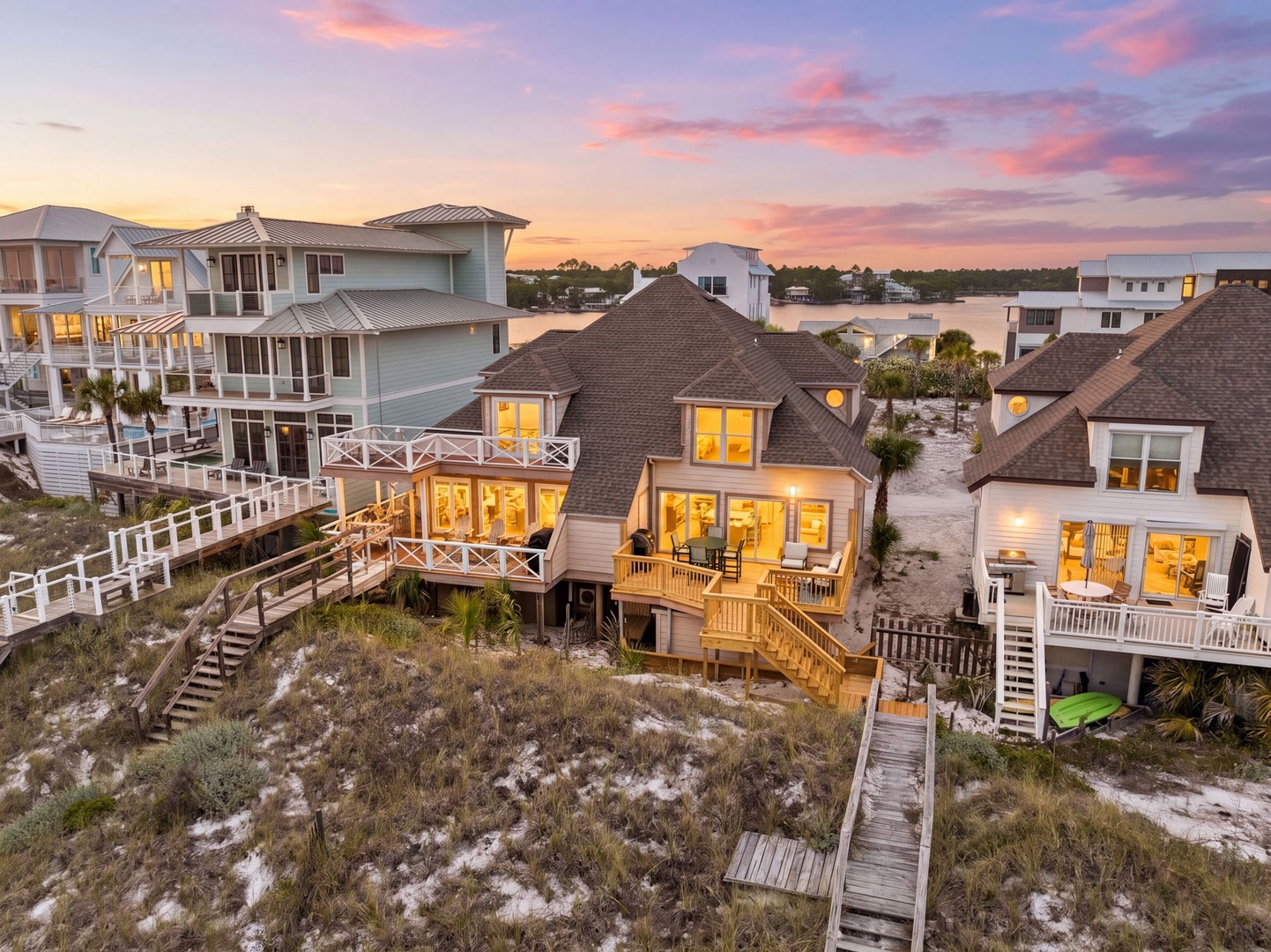 A stunning beachfront property nestled along a serene waterfront community, with sandy dunes and boardwalk access to the shore, beautifully illuminated at twilight.