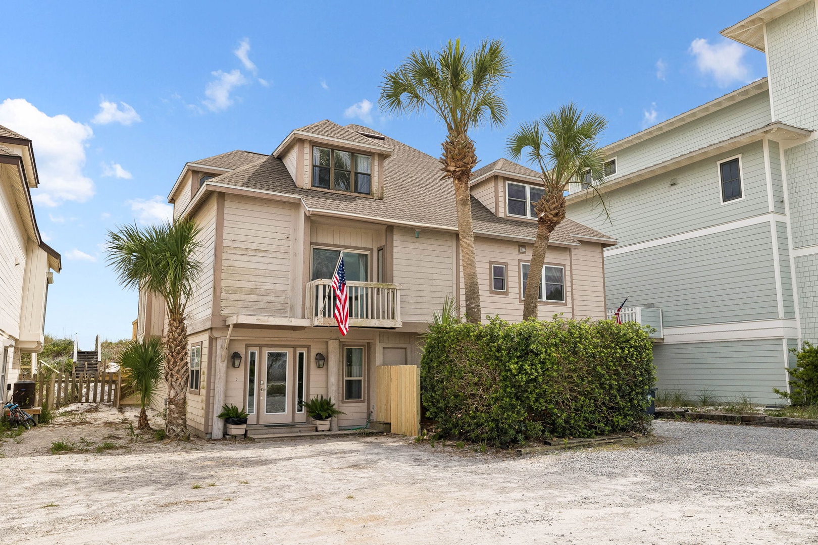 A welcoming coastal property with palm trees and a front balcony, situated in a quiet beachside neighborhood under sunny skies.