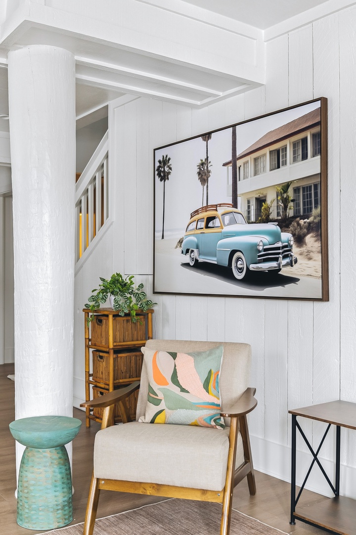 Your cozy reading nook awaits, featuring a mid-century armchair, vibrant coastal artwork, and thoughtful touches that make this space uniquely yours for relaxing.