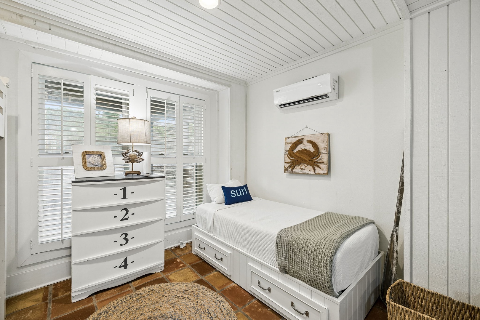 Your cozy coastal bedroom features crisp white linens, nautical accents, and a storage-smart bed. The vintage-inspired dresser and beachy crab art bring relaxed charm to this bright, comfortable space.