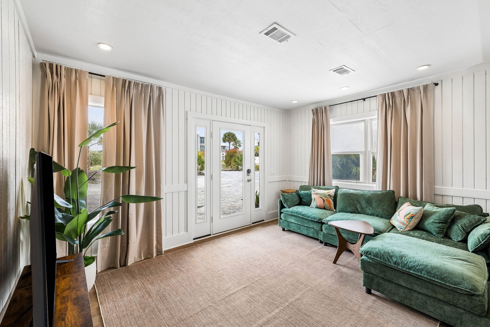 Sink into the plush emerald sofa and unwind in your bright, airy living room, where coastal charm meets comfort. Floor-to-ceiling windows invite natural light and serene outdoor views into your personal retreat.