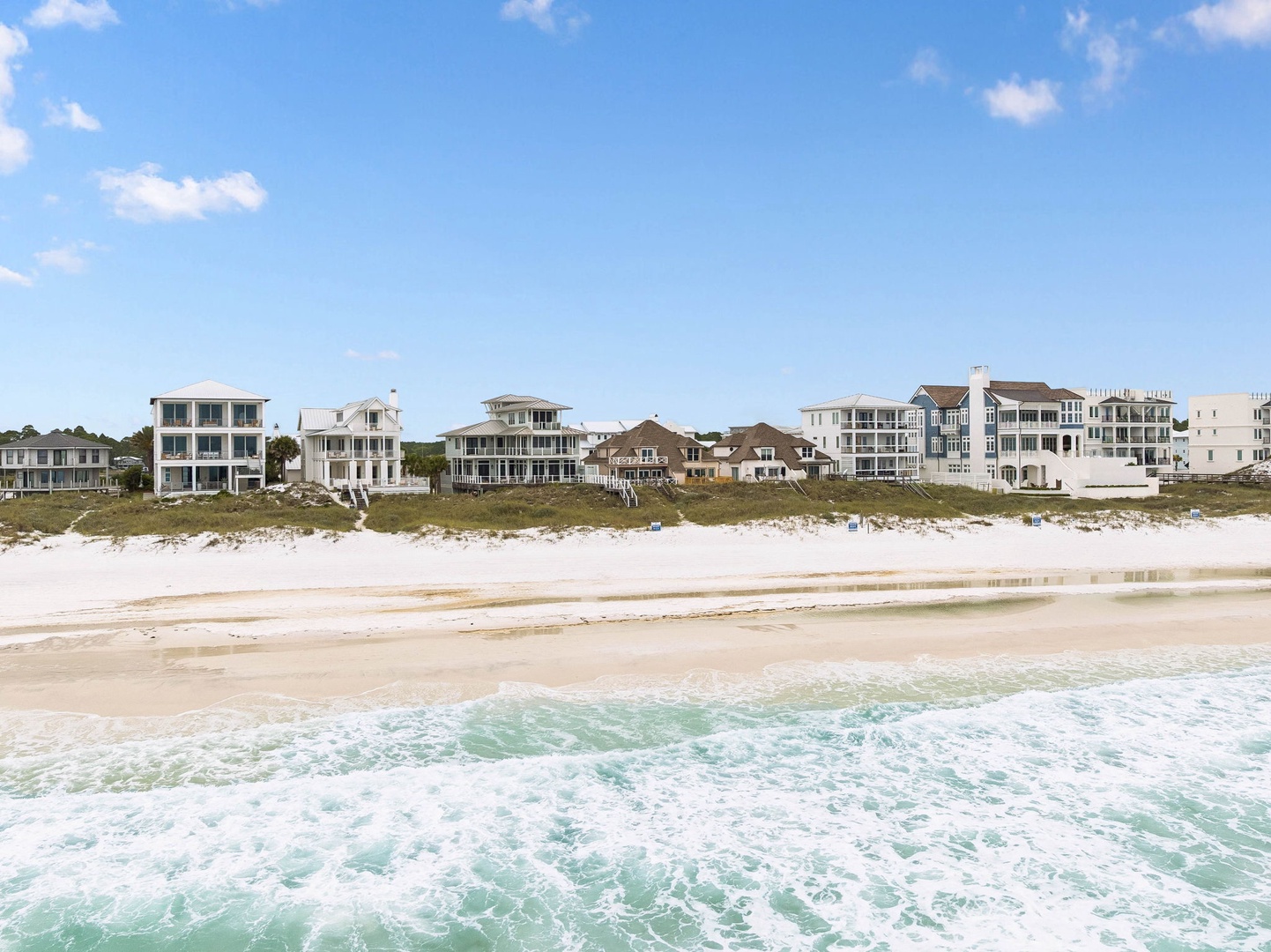 Beachfront vacation homes line the pristine white sand shore, offering direct access to crystal-clear turquoise waters and coastal living.