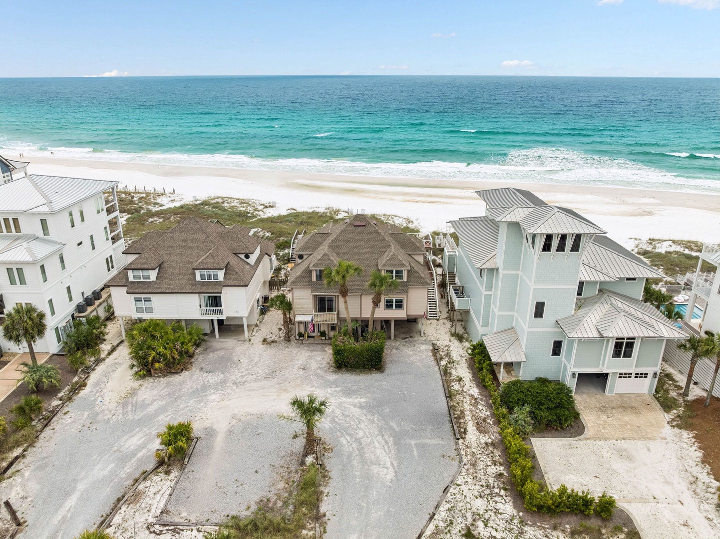 Beachfront vacation homes nestled along pristine white sand shores with turquoise gulf waters stretching to the horizon under a sunny sky.