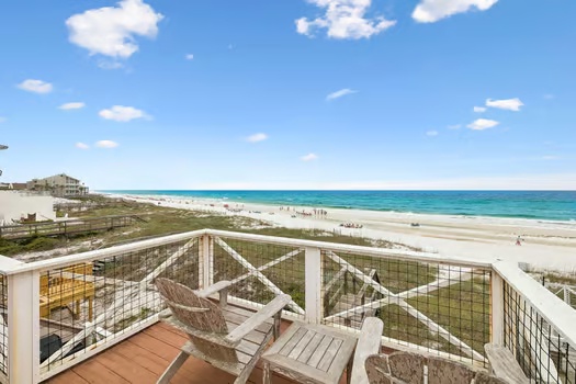 Private balcony overlooking pristine white sand beach and turquoise Gulf waters, with comfortable seating perfect for morning coffee or sunset views.