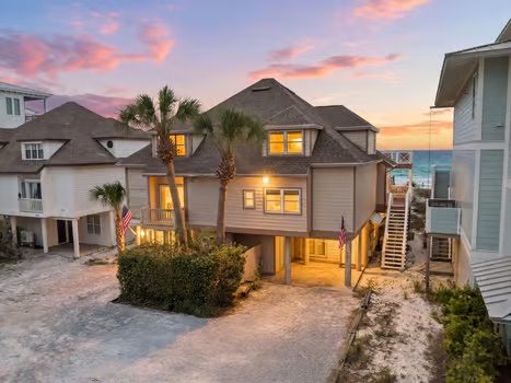 Coastal vacation rental home with palm trees and warm sunset skies in a quiet beachside neighborhood, offering easy access to nearby sandy shores.