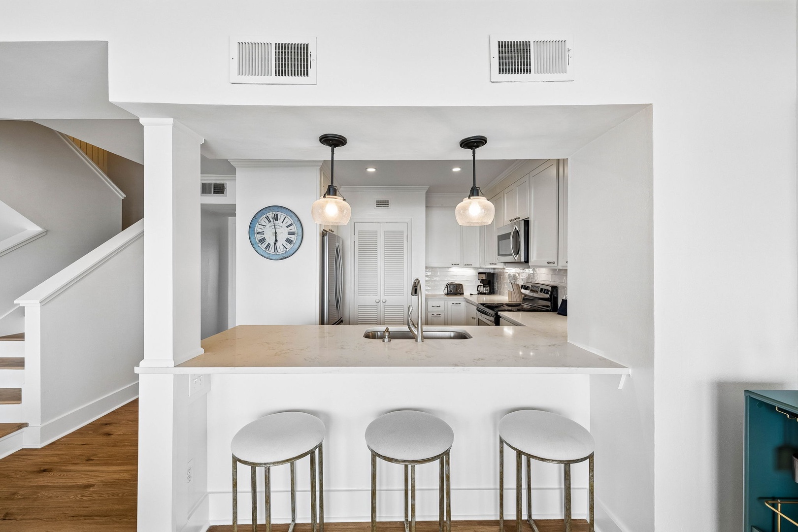 Your modern open-concept kitchen features sleek white cabinetry, stainless appliances, elegant pendant lighting, and a spacious breakfast bar—perfect for morning coffee or casual meals.