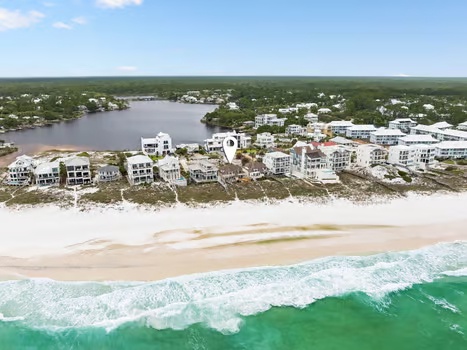 Aerial view of beachfront vacation properties nestled between pristine sandy shores and a peaceful coastal river, surrounded by lush natural landscape.