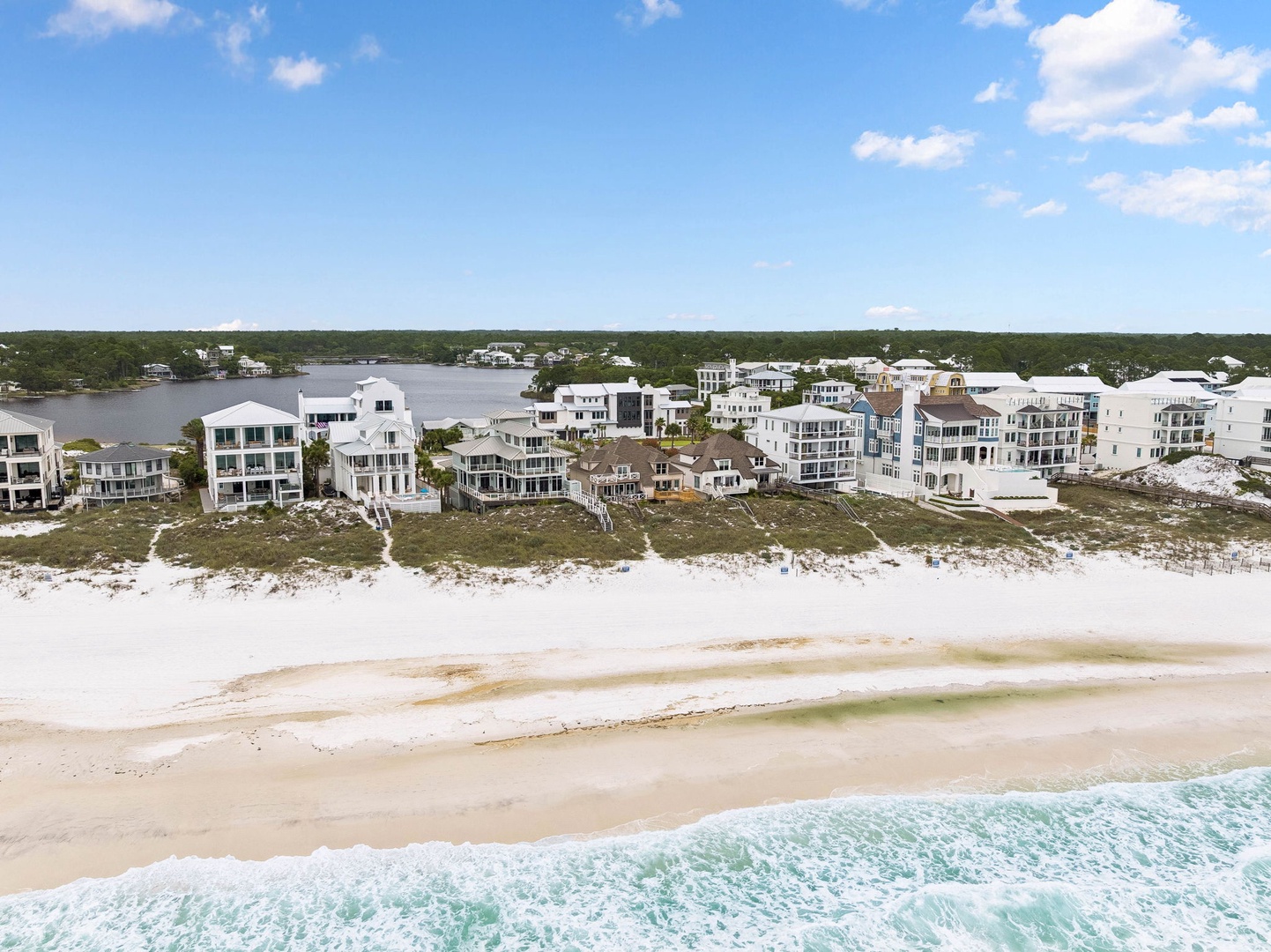 Aerial view of beachfront vacation homes nestled between pristine white sand beaches and tranquil waterways, showcasing the property's prime coastal location.