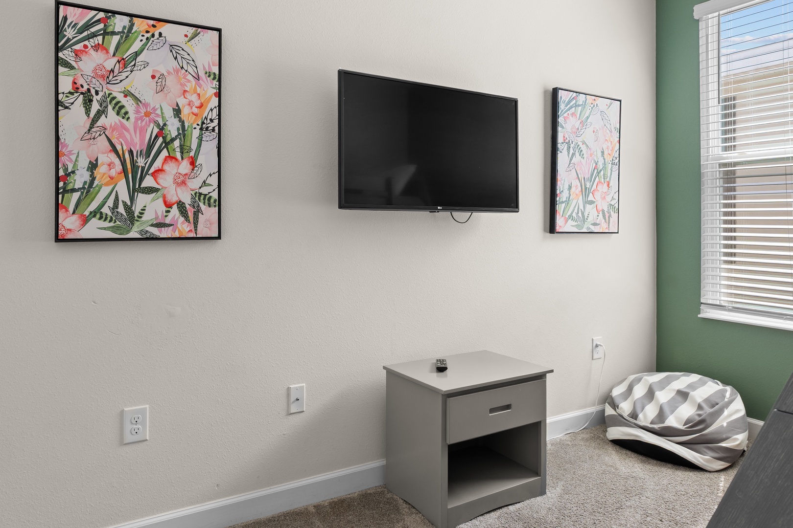Unwind in your comfortable bedroom with wall-mounted TV and cheerful botanical artwork creating a peaceful atmosphere.