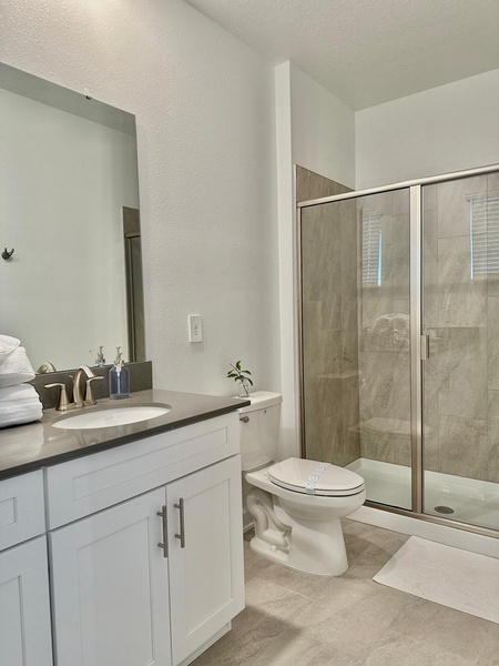 Step into your private spa-like bathroom featuring sleek modern finishes, spacious glass shower, and pristine white vanity.